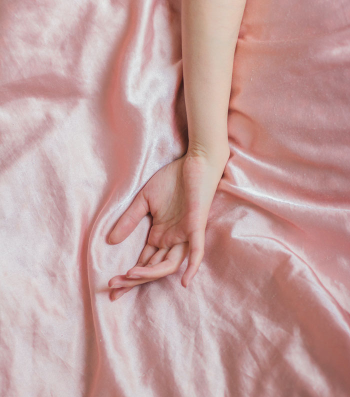 Woman hand on a pink bedsheet
