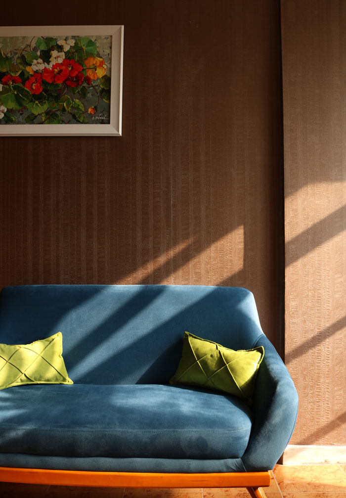 Blue velvet sofa with two yellow pillows in the brown interior with hanged picture