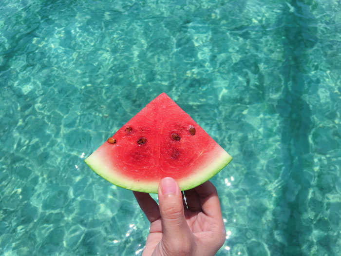 Hand holding a slice of watermelon in the water background