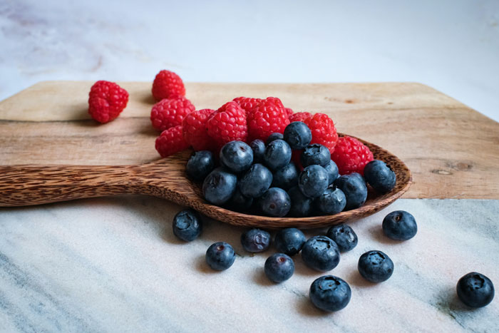 A wooden spoon with raspberries and blueberries on the table
