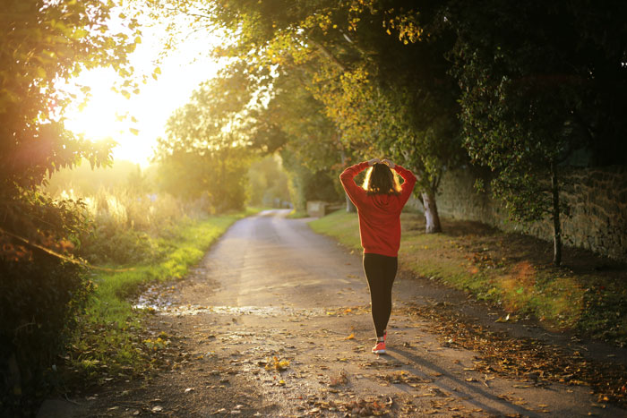 A woman with sportswear walking on the road in the forest