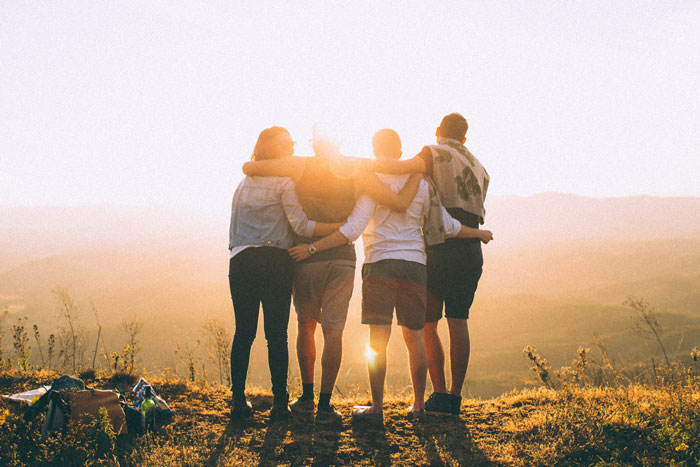 Four hugging friends standing in the mountain watching the sun