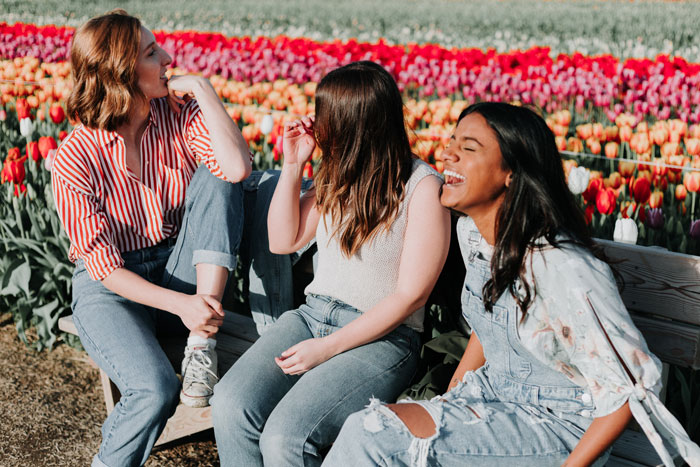 Three women sitting on the bench with a red tulip field in the background and laughing