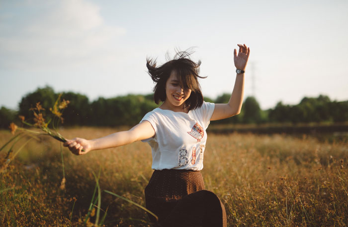 Black-haired young woman joyfully dancing in a field