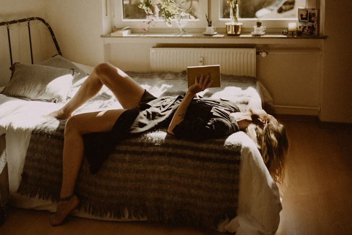 Woman with book in her hands lying on bed