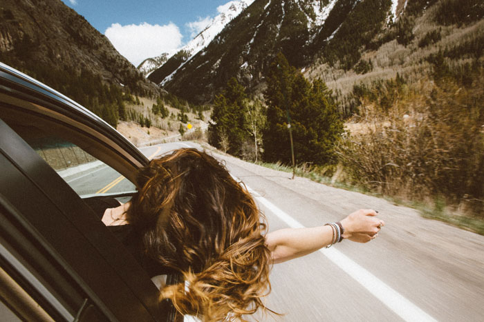 A woman riding in a car on a mountain road and taking her hand and head out of the car window 
