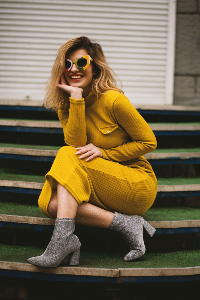 A happy woman in a yellow outfit and funky sunglasses posing on the stairs