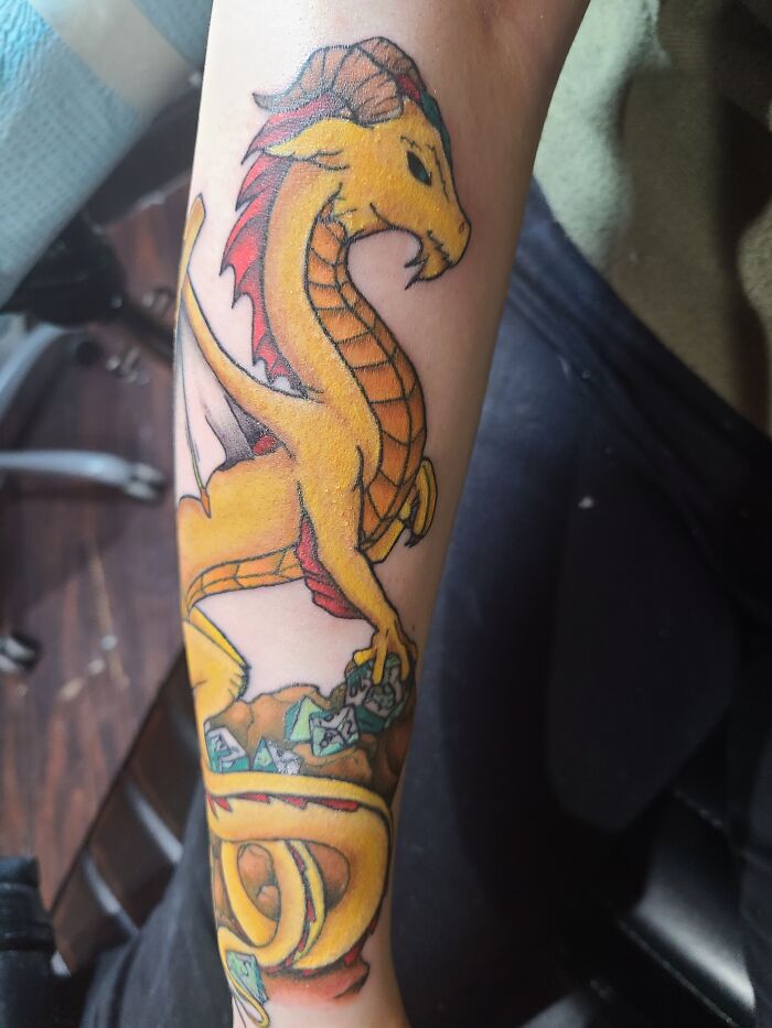 Yellow dragon tattoo with orange scales and red details on an arm, showcasing cool artistic design.