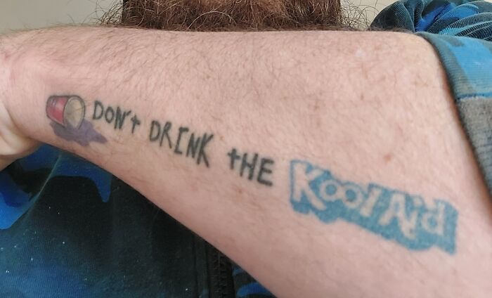 Forearm tattoo of a cup and text reading "Don't Drink the Kool-Aid," blending humor and a cautionary message.