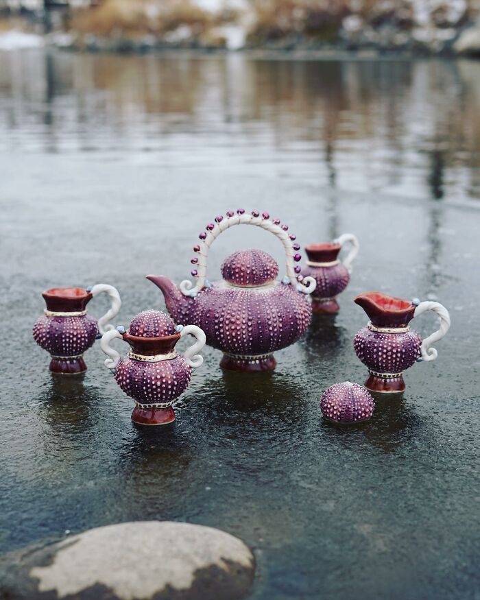 Nature-inspired ceramics set with textured purple design placed on a reflective wet surface.