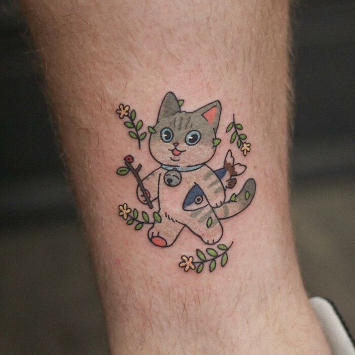 Animal-themed tattoo design of a cartoon cat with flowers, created by a tattoo artist.