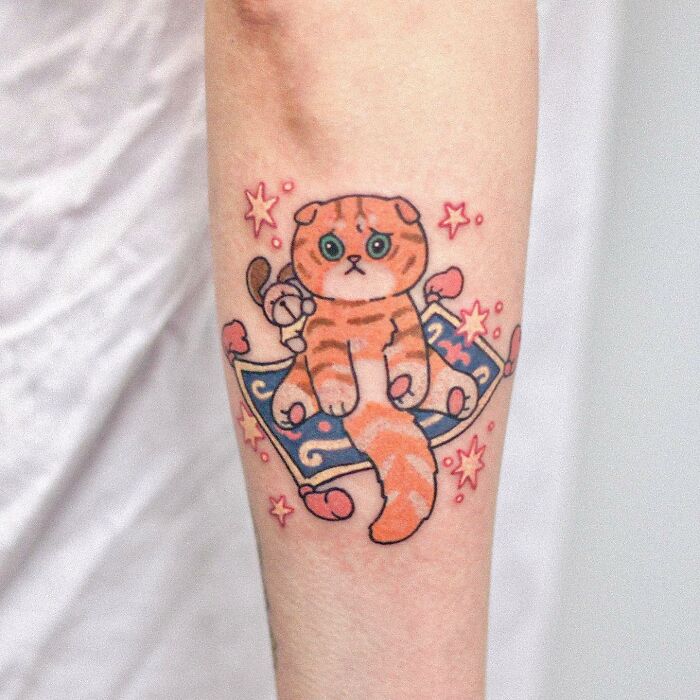 Tattoo of an adorable orange cat on a magic carpet, surrounded by stars, showcasing animal-themed design.