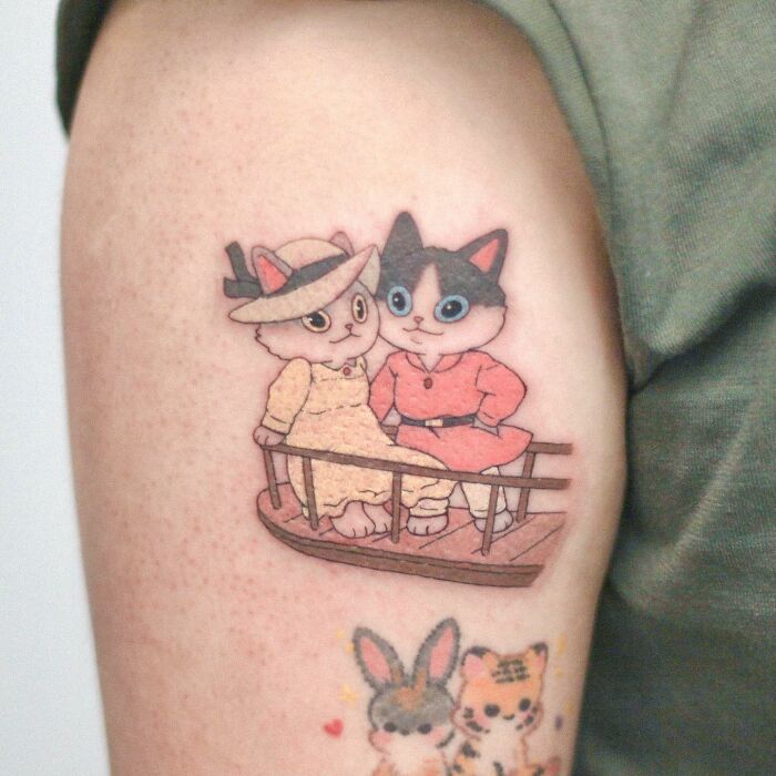 Adorable animal-themed tattoo of cartoon cats in outfits on an arm.