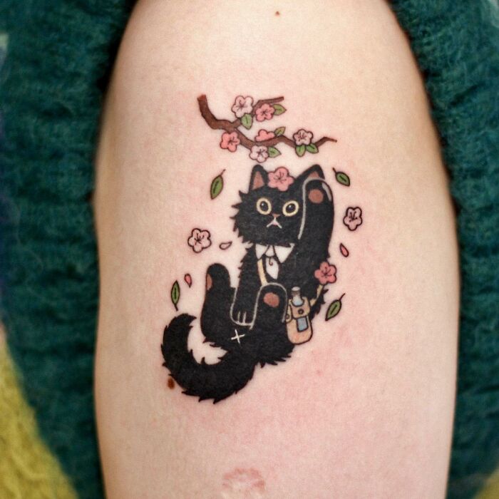 Adorable animal-themed tattoo with a black cat and cherry blossoms on a person's arm.