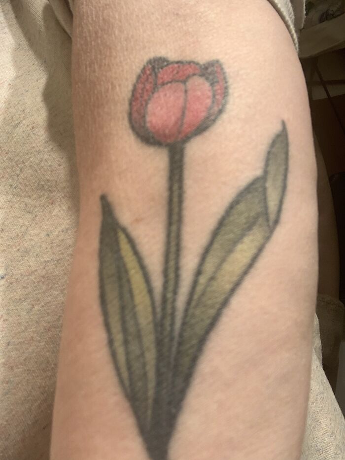 Arm tattoo of a red tulip with green leaves.