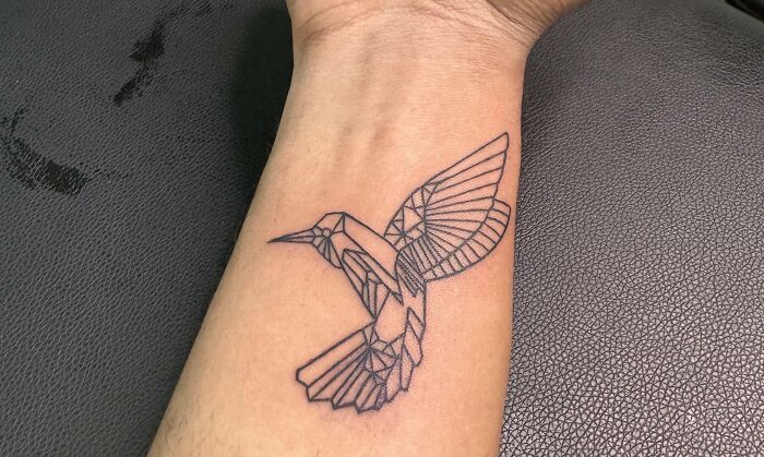 Geometric tattoo of a bird with angular designs on a person's forearm.