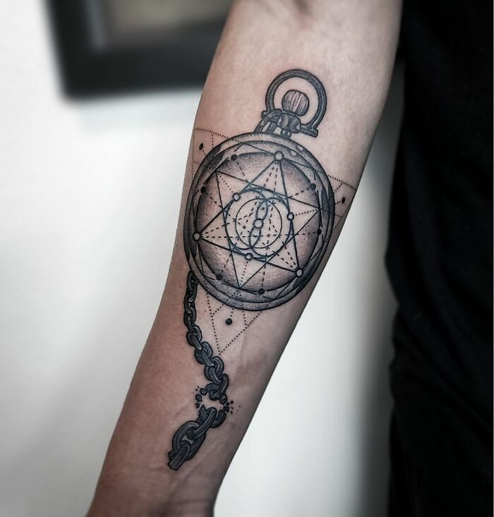 Geometric tattoo of a pocket watch with intricate patterns on the forearm.