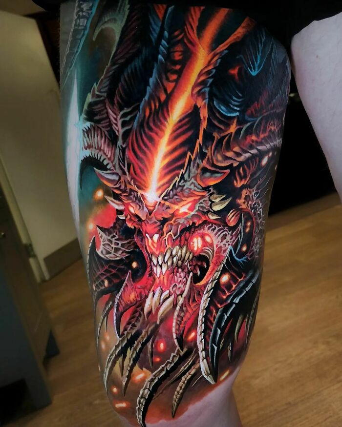 Realistic tattoo of a fiery demonic creature with intricate details and vibrant colors on a person's leg.
