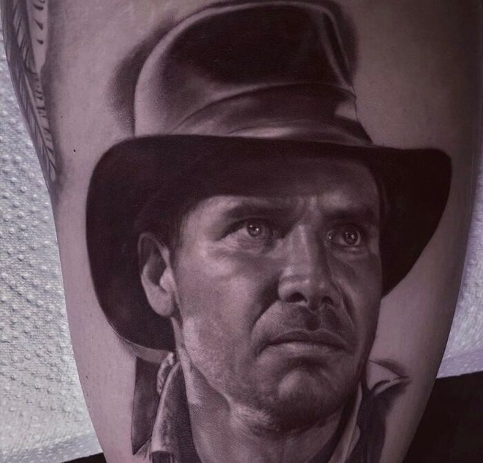 A super realistic tattoo of a man wearing a hat, showcasing detailed facial features on the skin.