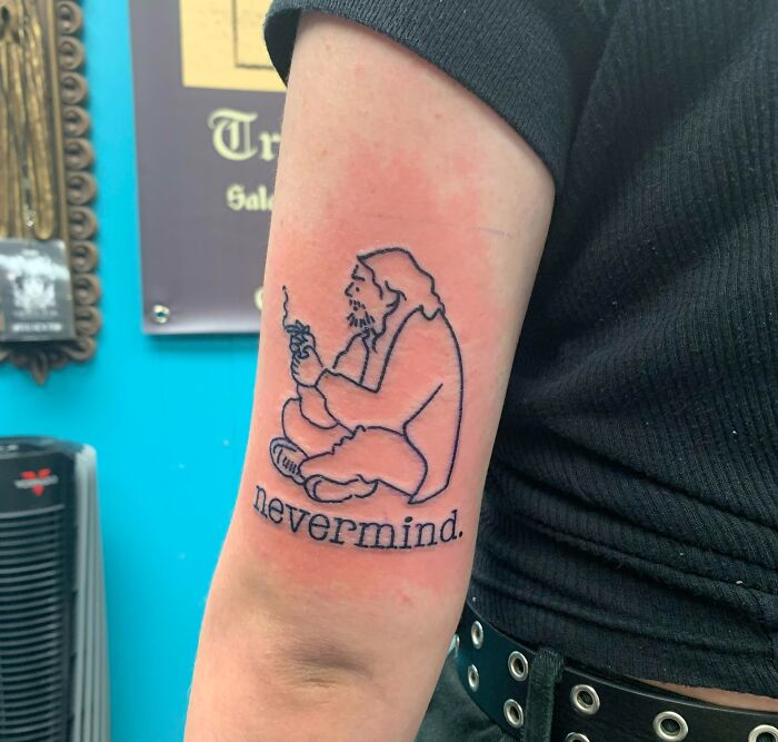 Line drawing tattoo with figure and "nevermind" text on arm, showcasing word tattoo art.