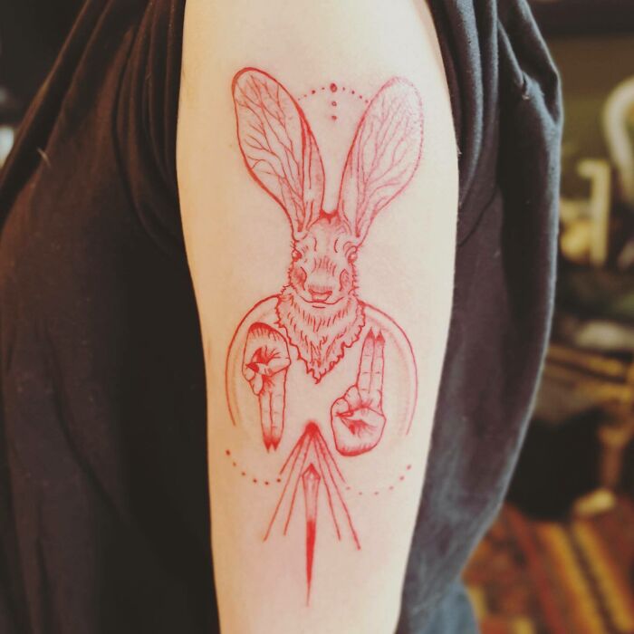 Red ink tattoo of a jackalope with intricate design on a person's upper arm.