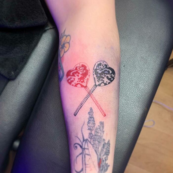 Red ink heart lollipop tattoos on arm, showcasing bold color and intricate design.