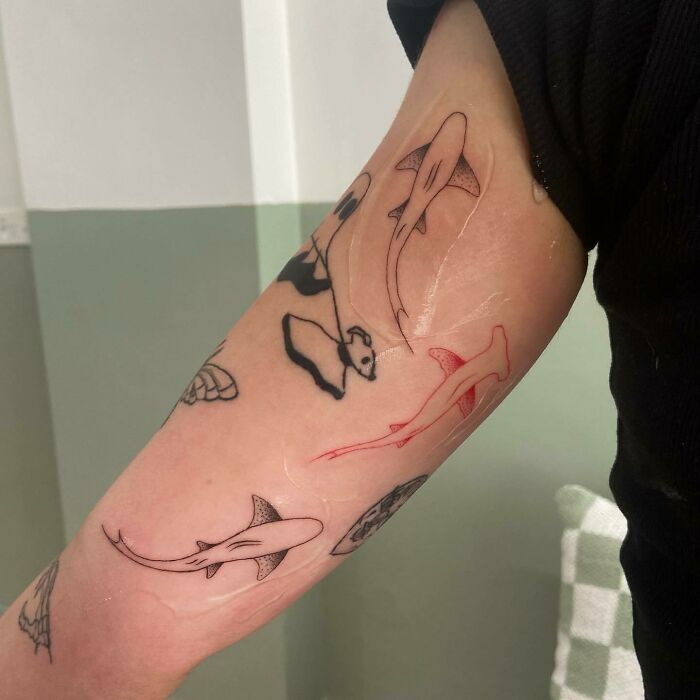 Red ink shark tattoo on forearm among other black ink designs, showcasing unique and vibrant tattoo art.