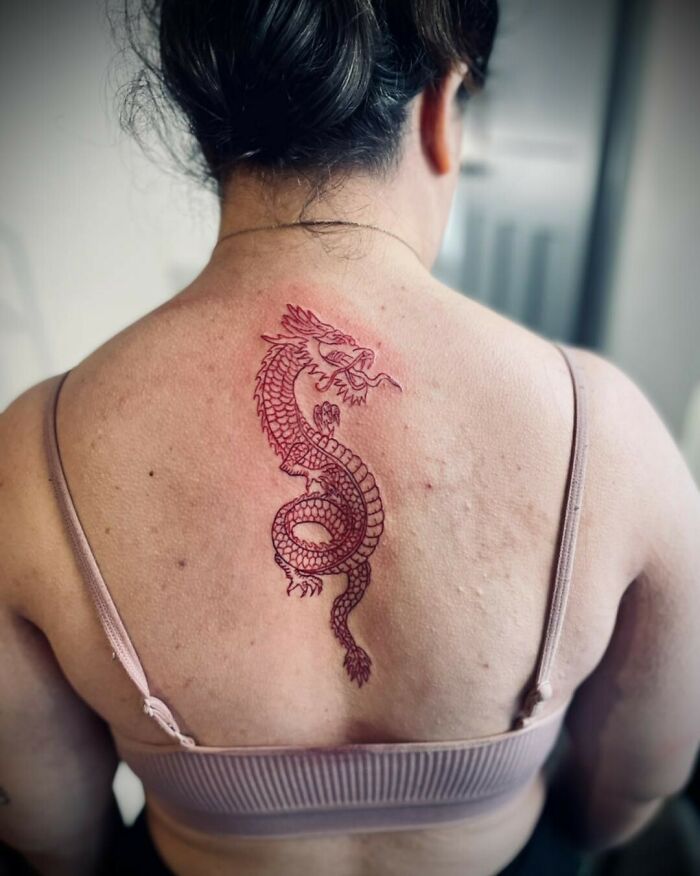 A red ink tattoo of a dragon on a person's back, showcasing intricate details.