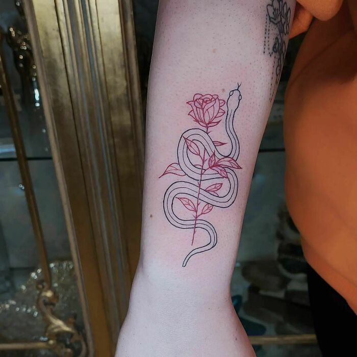 Red ink tattoo of a snake entwined with a rose on a person's forearm.