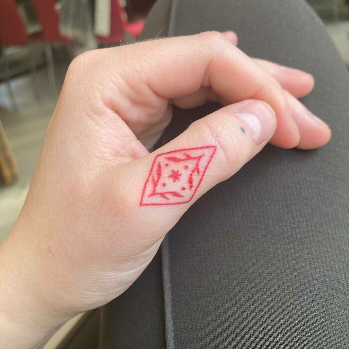 Red ink tattoo of a geometric star design on a thumb, showcasing a showstopping style.