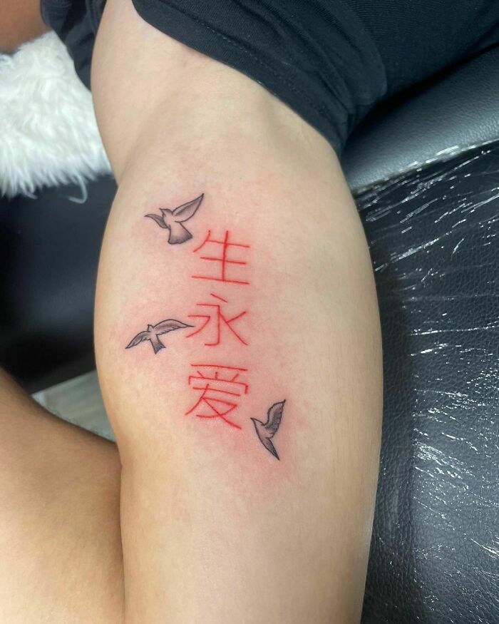 Red ink tattoo with Chinese characters and birds on an upper arm.
