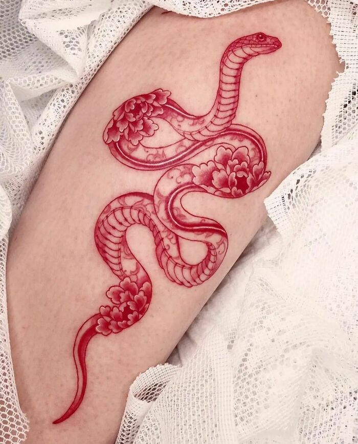 Red ink tattoo of an intricate snake design on skin, surrounded by white lace.