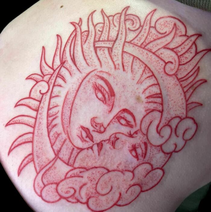 Red ink tattoo depicting a sun and moon design with intricate line work and shading.