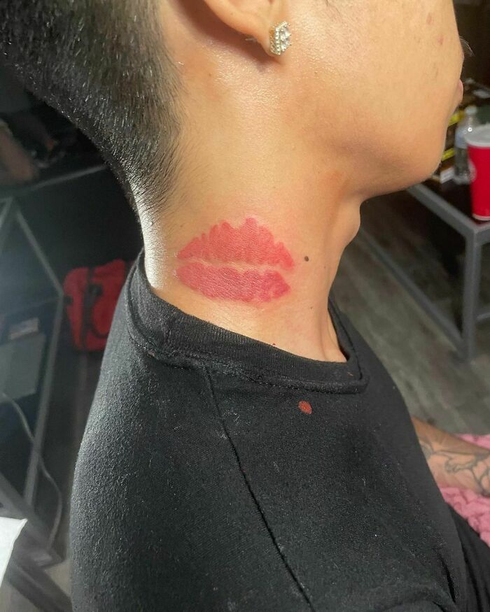 Red ink tattoo of lips on neck under ear, showcasing vibrant color and artistic design.