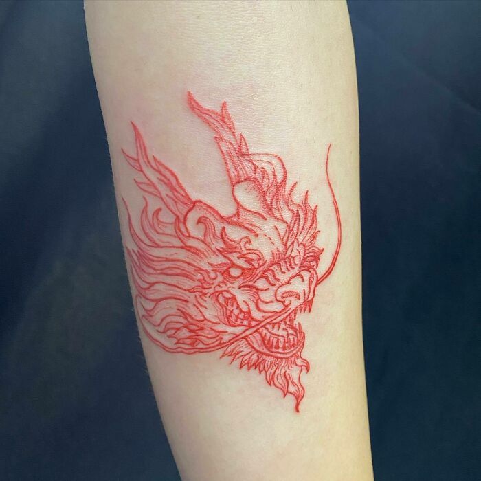 Red ink dragon tattoo design on forearm, showcasing intricate details and bold lines.