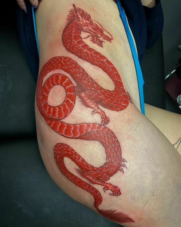Red ink tattoo of a dragon intricately designed on a person's thigh, showcasing vibrant artistry.
