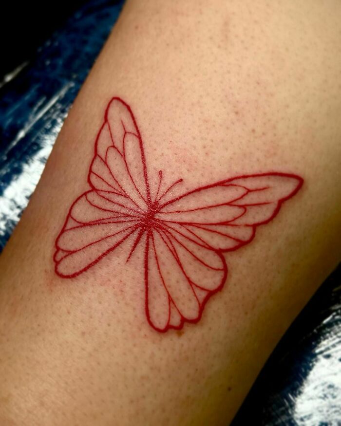 Red ink butterfly tattoo on skin, showcasing intricate line work and vibrant color.