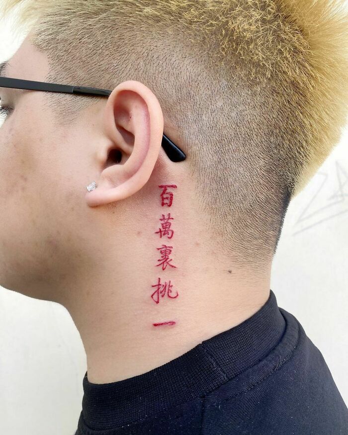 Red ink tattoo with vertical Asian characters on the side of a neck, next to an ear with an earring.