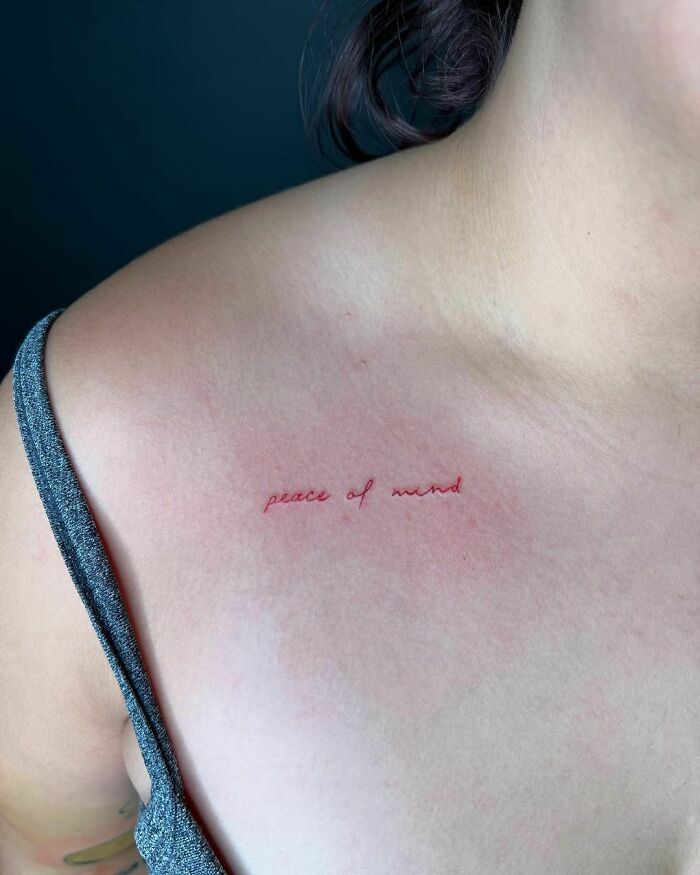 Red ink tattoo on collarbone with "peace of mind" text, showcasing minimalist design.