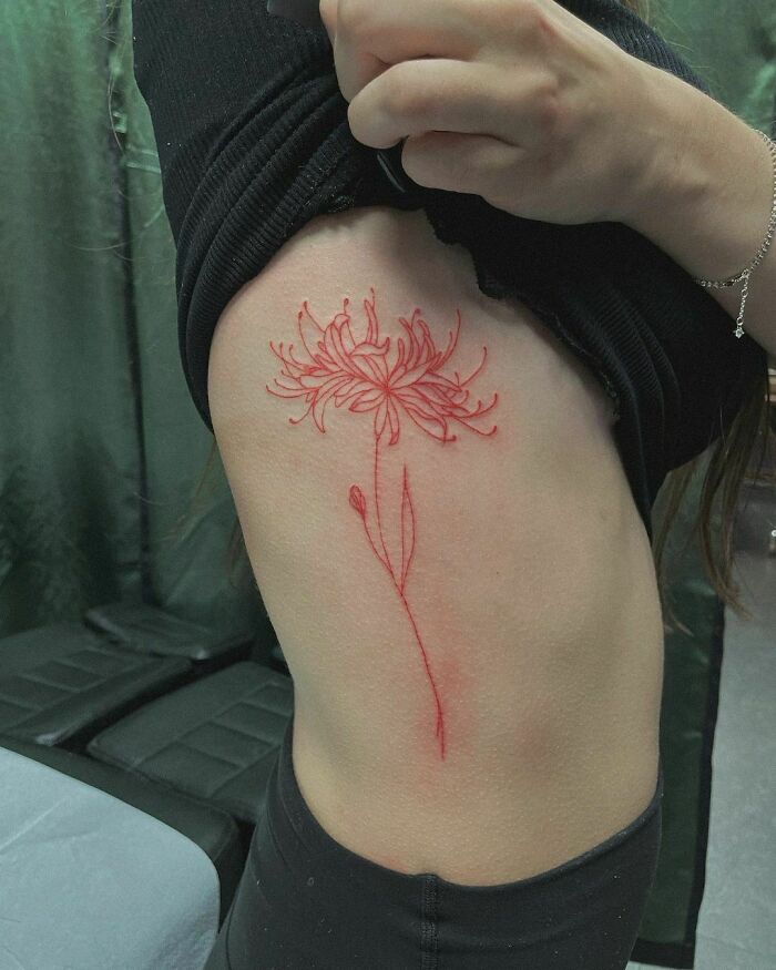Red ink tattoo of a flower on someone's side, showcasing intricate line work.