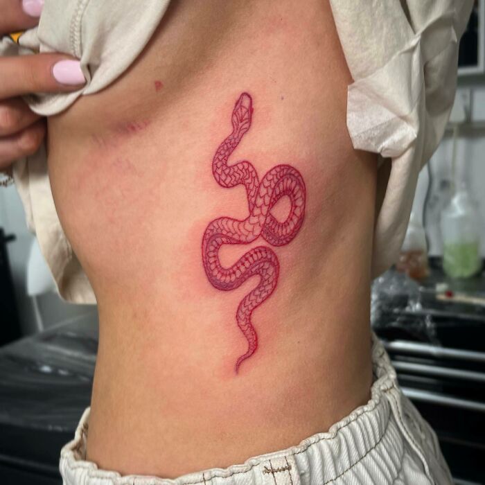 Red ink snake tattoo on a person's side, showcasing intricate detailing and vivid color.