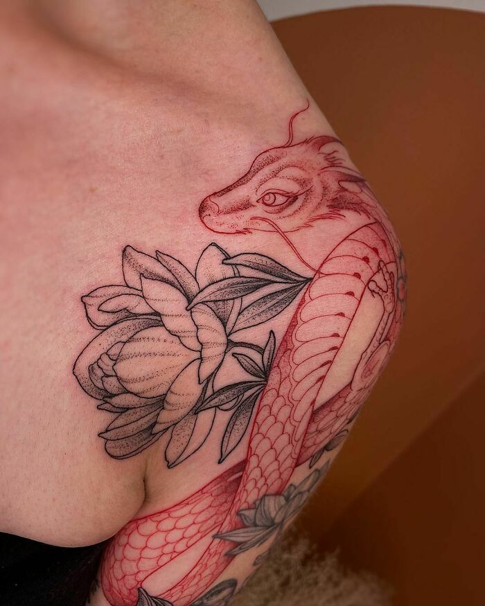 Red ink tattoo featuring a dragon and peony design on a shoulder, highlighting intricate details and artistry.