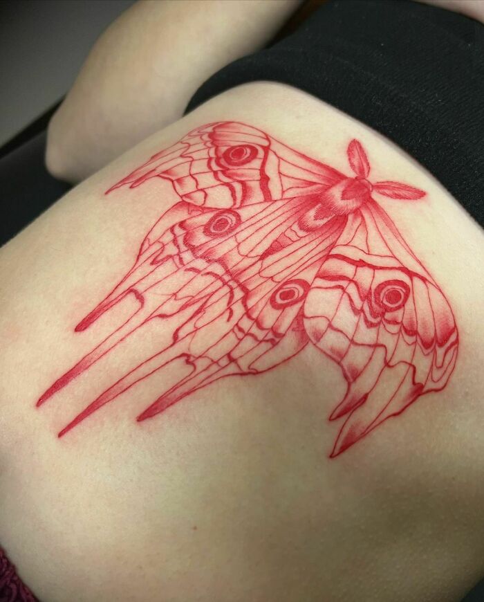 Red ink tattoo of an intricate moth design on skin.