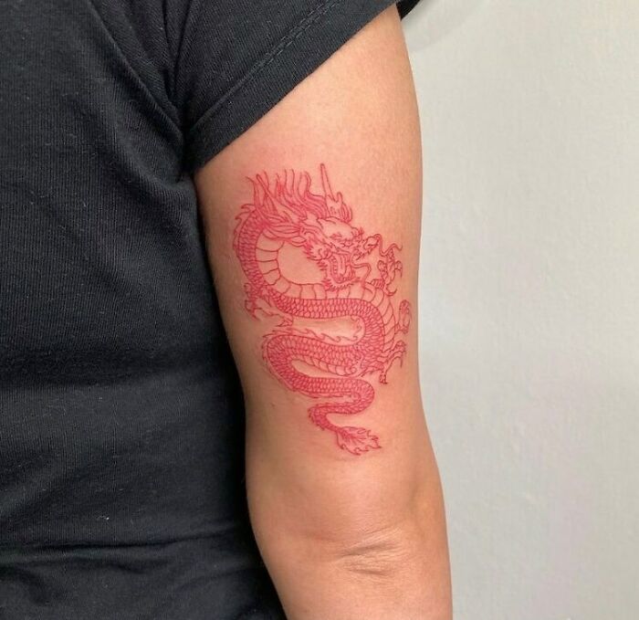 Red ink dragon tattoo on upper arm, showcasing intricate design.