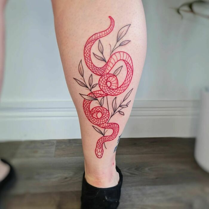 Red ink tattoo of a snake with leaves on a person's leg.