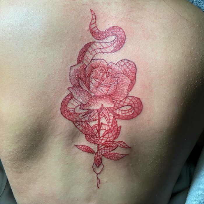 Red ink tattoo of a rose and snake entwined on skin, showcasing intricate design.