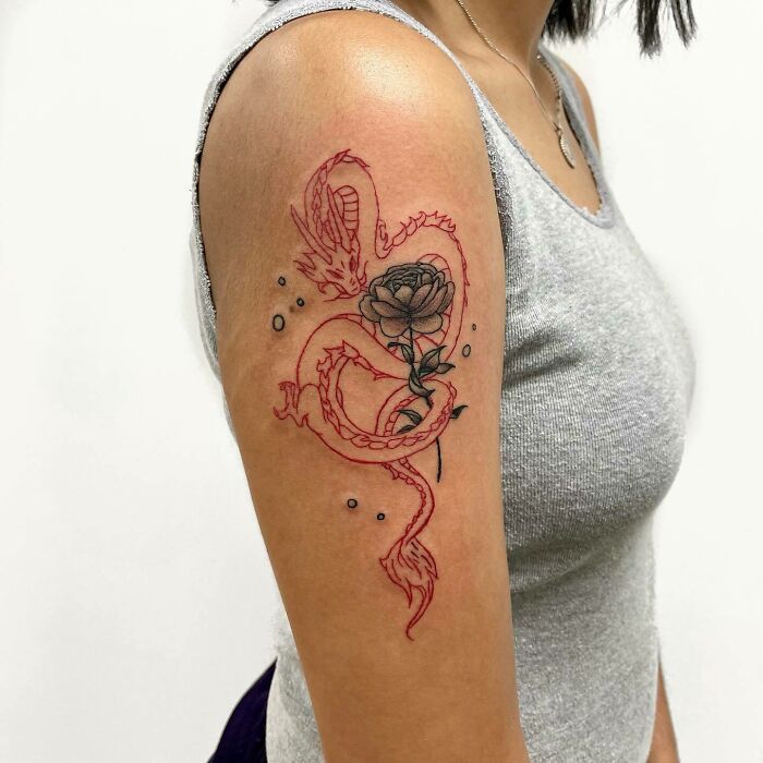 Red ink tattoo of a dragon intertwined with a black flower on a person's arm, showcasing intricate design and bold colors.