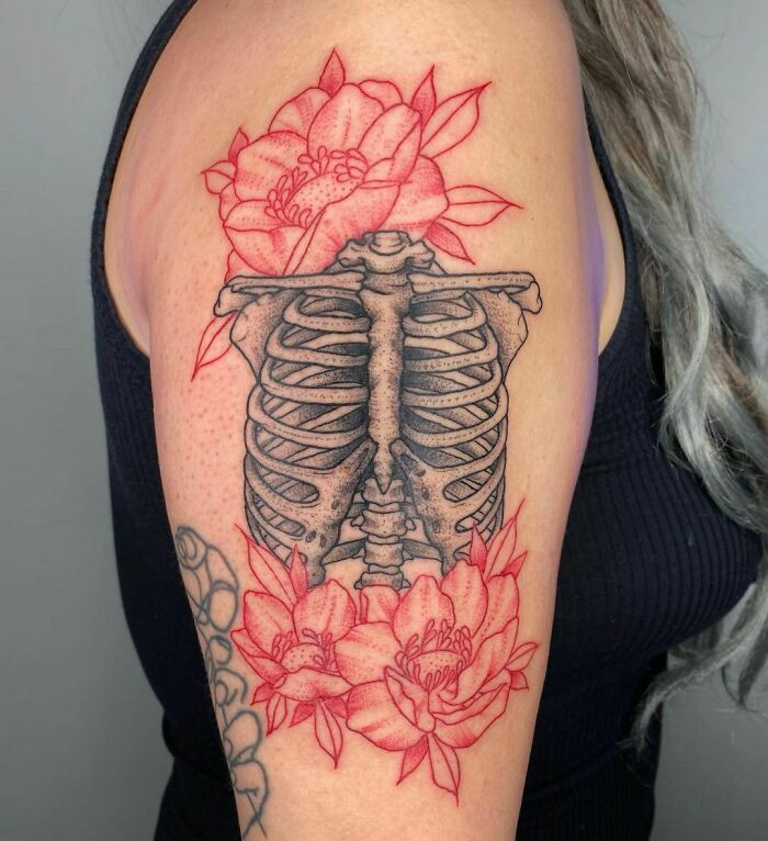 Red ink tattoo on arm featuring ribcage and blooming flowers, showcasing intricate design details.