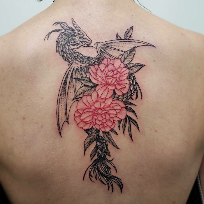Red ink tattoo of a dragon intertwined with flowers on a person's back.
