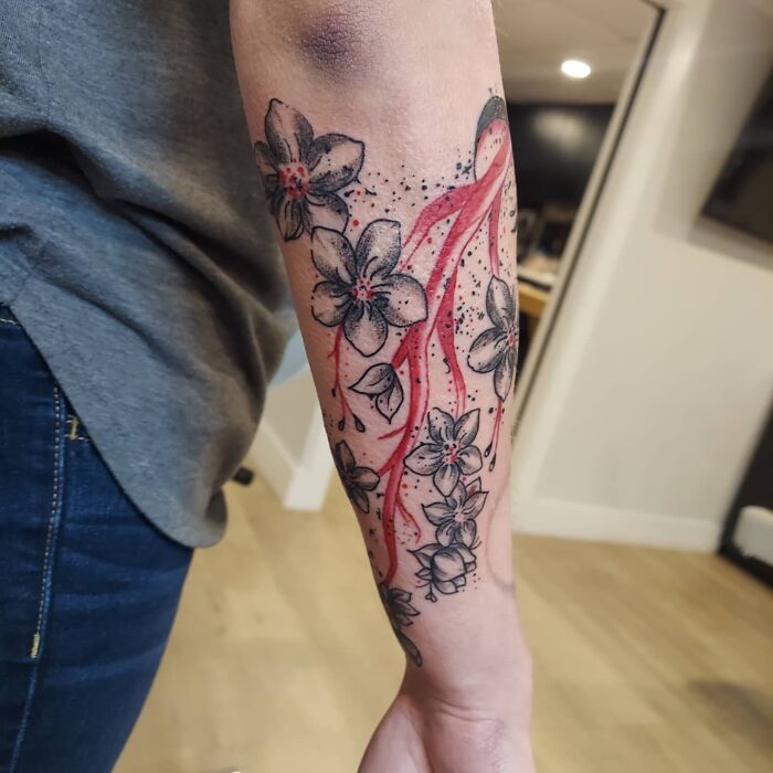 Red ink tattoo of flowers and abstract design on an arm, featuring intricate details and bold red accents.